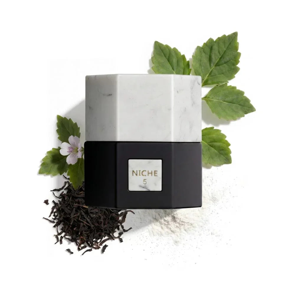 Niche 5 perfume bottle with marble design, green leaves, and dried tea leaves on white background