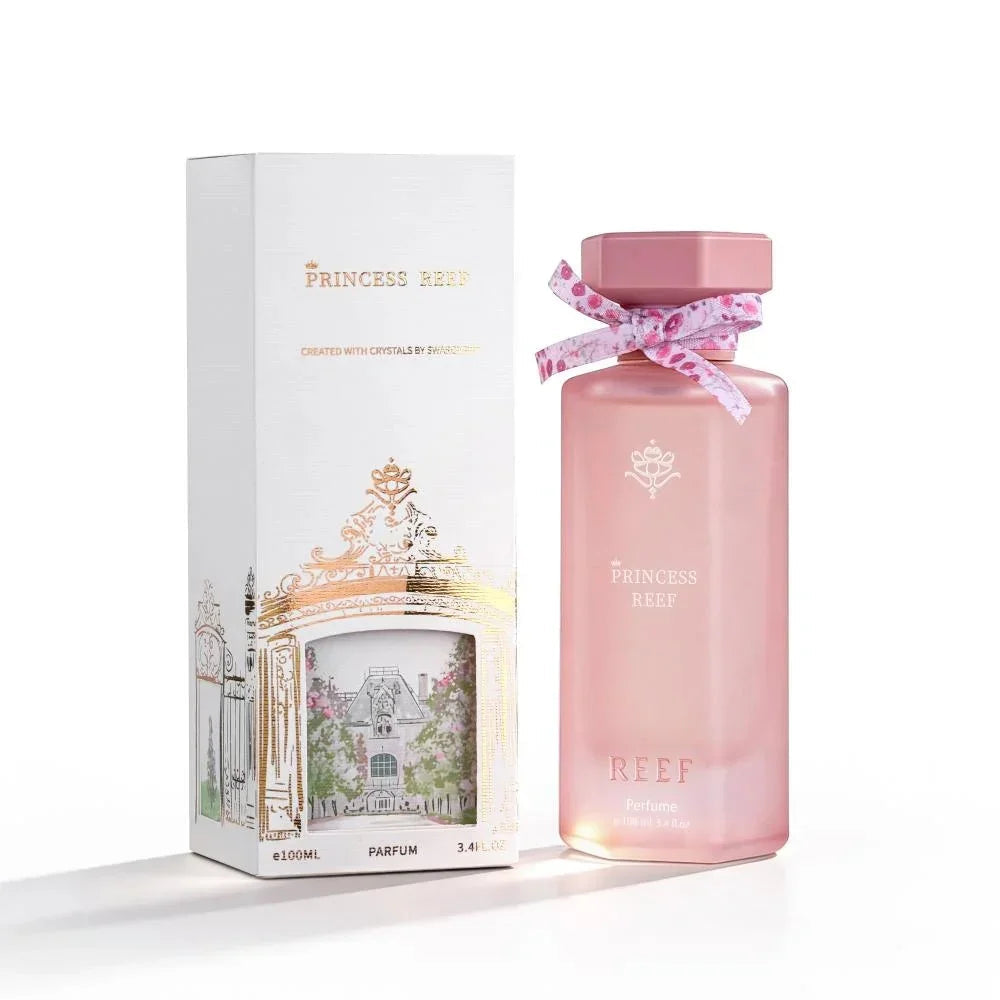 Pink Princess Reef perfume bottle with floral ribbon, beside elegant white box featuring gold accents and garden illustration
